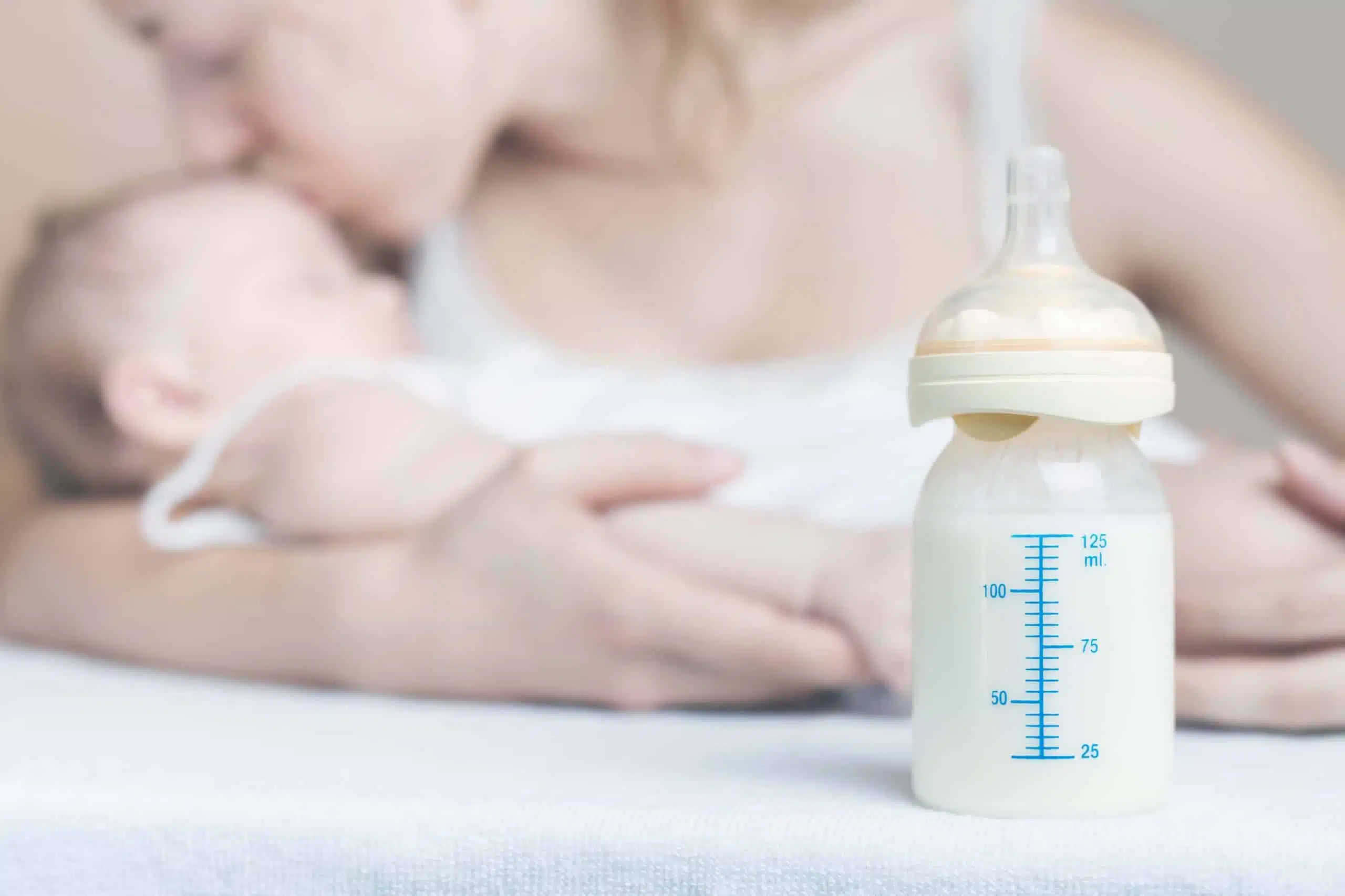 אמא ותינוק ברקע ובפוקוס בקבוק עם חלב