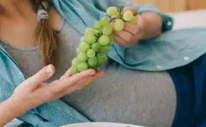 אישה בהריון שוכבת על המיטה ואוכלת ענבים