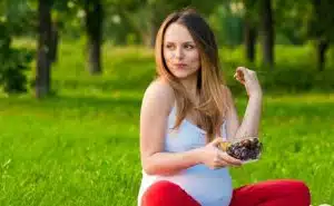אשה בהריון יושבת בפארק ואוכלת קערה עם פירות