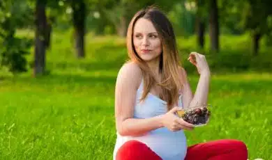 אשה בהריון יושבת בפארק ואוכלת קערה עם פירות