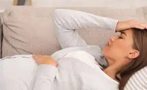 אישה בהריון שוכבת בספה ומחזיקה בבטן ובראש שלה