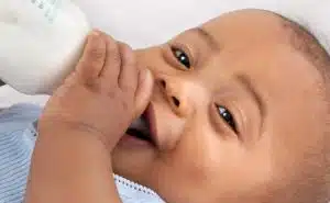 תינוק שוכב, מחייך ושותה בקבוק עם חלב
