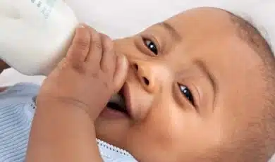תינוק שוכב, מחייך ושותה בקבוק עם חלב