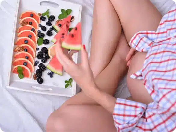 אישה בהריון יושבת ולידה מגש עם פירות