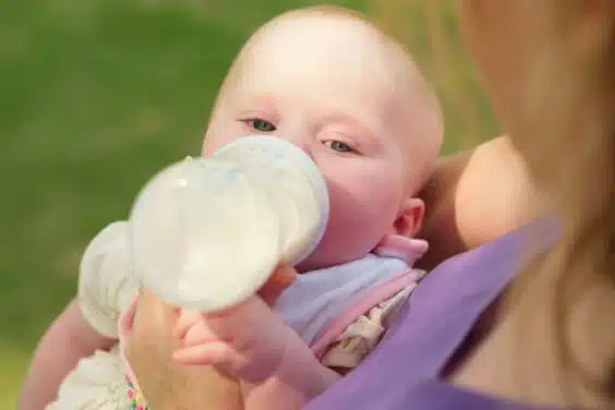 תינוקת שותה בקבוק חלב עם סינר