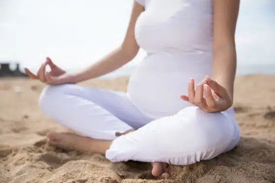 קלוזאפ על אישה בהריון עושה יוגה על חוף הים