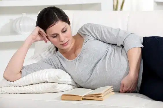 אישה בהריון שוכבת על המיטה וקוראת ספר