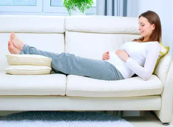 אישה בהריון שוכבת על הספה ומרימה רגליים להקלה על בצקות