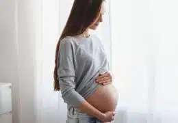 אישה בהריון עם הידיים על הבטן מסתכלת מהחלון
