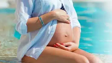 אישה בהריון יושבת על שפת הבריכה