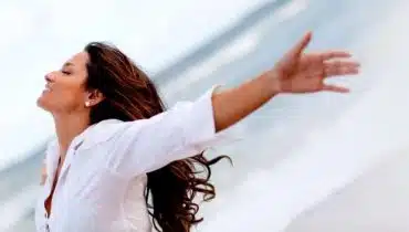 אישה לבושה בלבן עומדת על חוף הים עם ידיים פתוחות