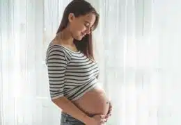 אישה בהריון ליד החלון מחזיקה את הבטן