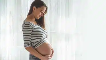 אישה בהריון ליד החלון מחזיקה את הבטן