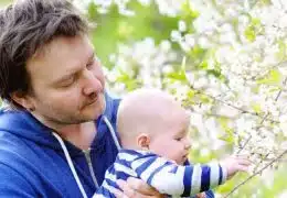 אבא מחזיק בתינוק שנוגע בפרחים על העץ