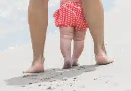 תינוקת מצולמת מאחור, הולכת עם אמא על חוף הים