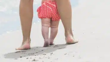 תינוקת מצולמת מאחור, הולכת עם אמא על חוף הים