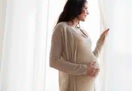 אישה בהריון מסתכלת בחלון ושמה יד על הבטן