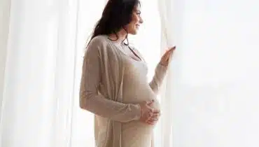 אישה בהריון מסתכלת בחלון ושמה יד על הבטן