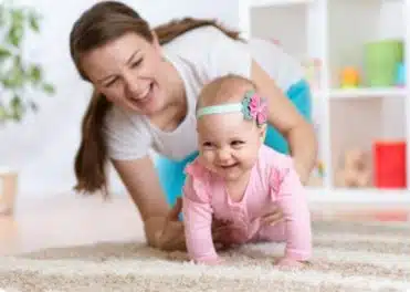 תינוקת זוחלת על השטיח ליד אמא