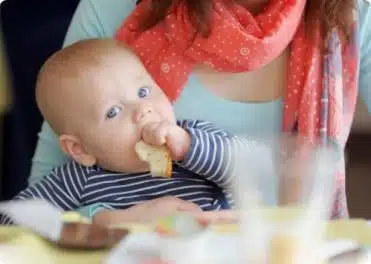 תינוק יושב על אימו ואוכל לחם