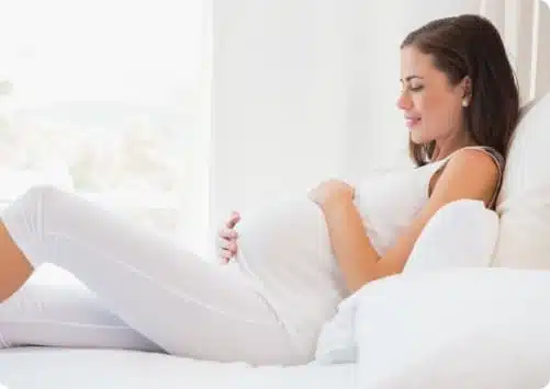 אישה בהריון שוכבת על המיטה ומניחה ידיים על הבטן שלה