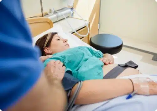 אישה בהריון מאושפזת בבית חולים ובעלה עומד ליד מיטתה ומחזיק בידה